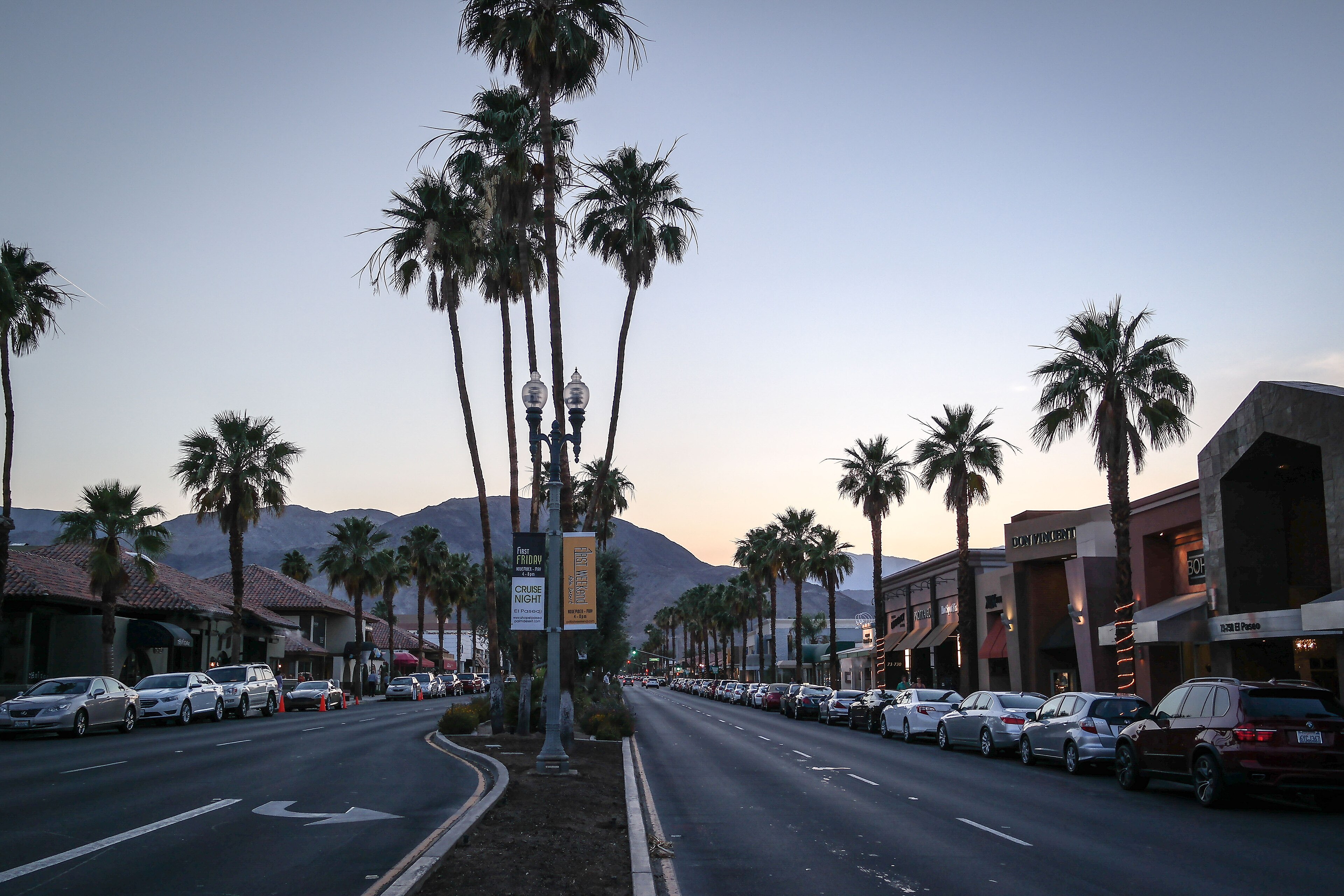 El Paseo in Palm Desert at dusk with palm trees, storefronts and the Santa Rosa Mountains behind